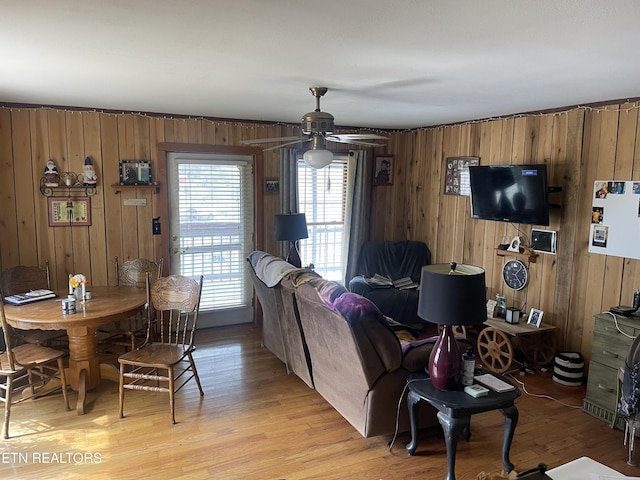 living area with wooden walls, a ceiling fan, and light wood-style floors