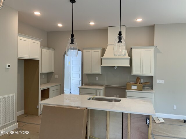 kitchen with a center island with sink, custom exhaust hood, visible vents, baseboards, and white cabinets