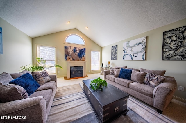 living area with lofted ceiling, a fireplace with flush hearth, a healthy amount of sunlight, and carpet floors