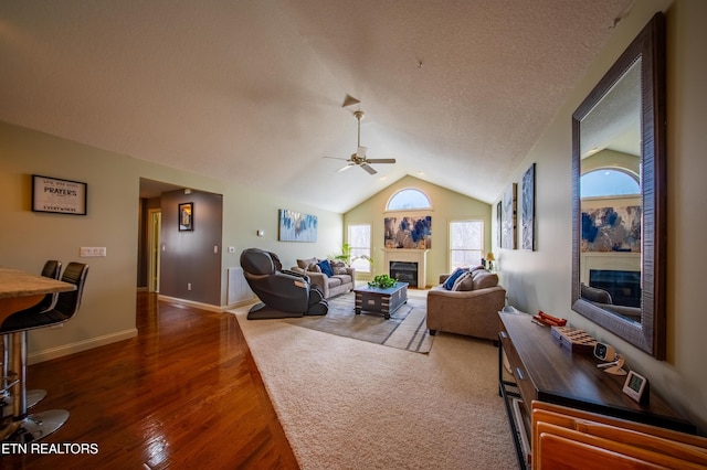 living room featuring a textured ceiling, a glass covered fireplace, wood finished floors, lofted ceiling, and ceiling fan