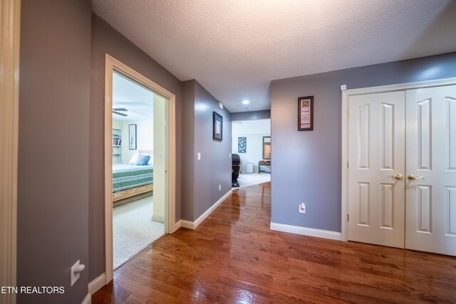 hallway featuring baseboards, a textured ceiling, and wood finished floors