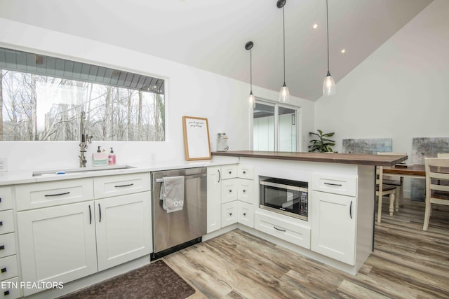 kitchen with a sink, stainless steel appliances, light wood-style flooring, and vaulted ceiling