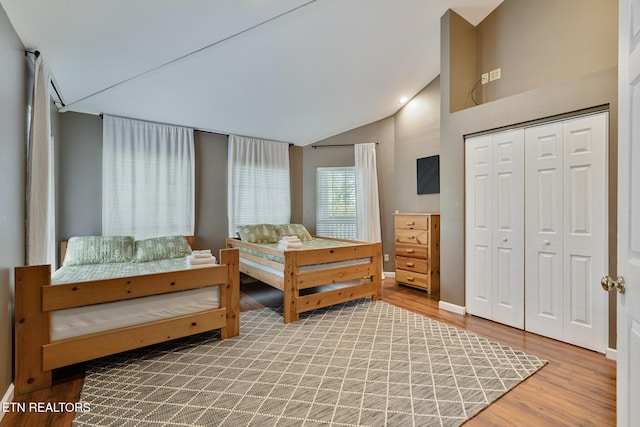 bedroom with a closet, baseboards, lofted ceiling, and wood finished floors