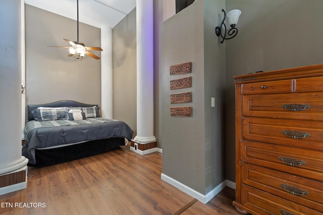 bedroom featuring ornate columns, baseboards, and wood finished floors