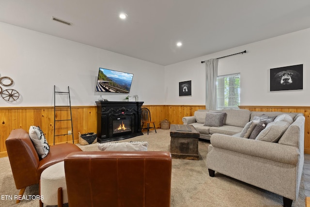living area featuring wooden walls, visible vents, a wainscoted wall, a glass covered fireplace, and carpet flooring