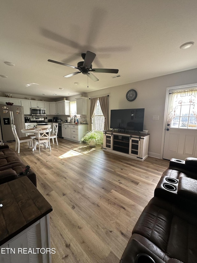 living area with visible vents, ceiling fan, baseboards, and light wood-style floors