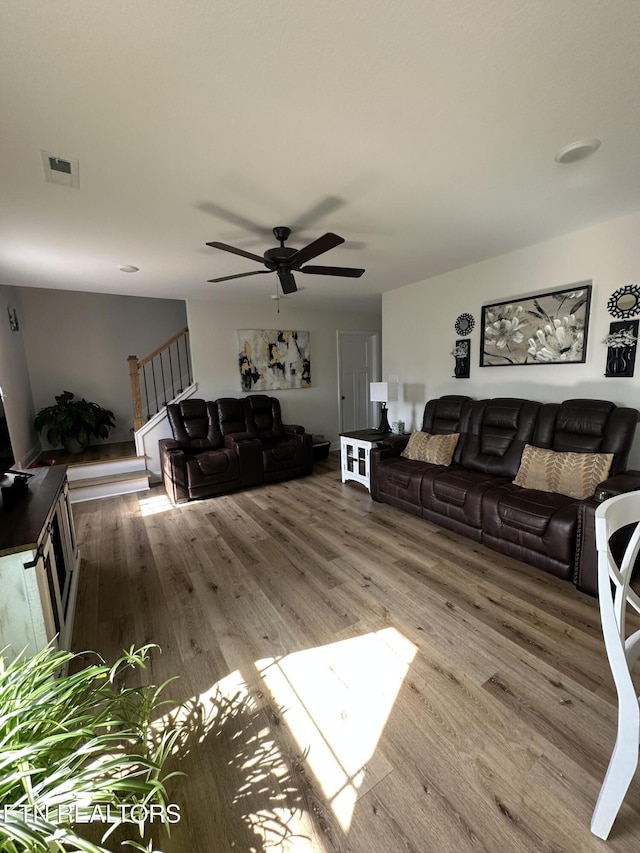living room with visible vents, stairway, ceiling fan, and wood finished floors