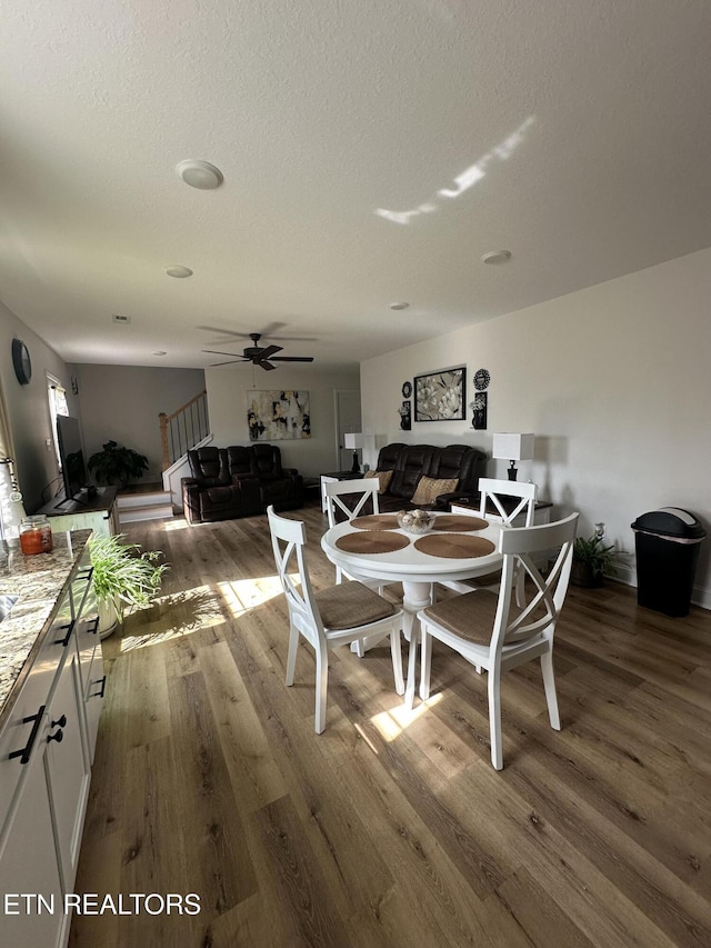 dining room with a ceiling fan, wood finished floors, stairs, and a textured ceiling