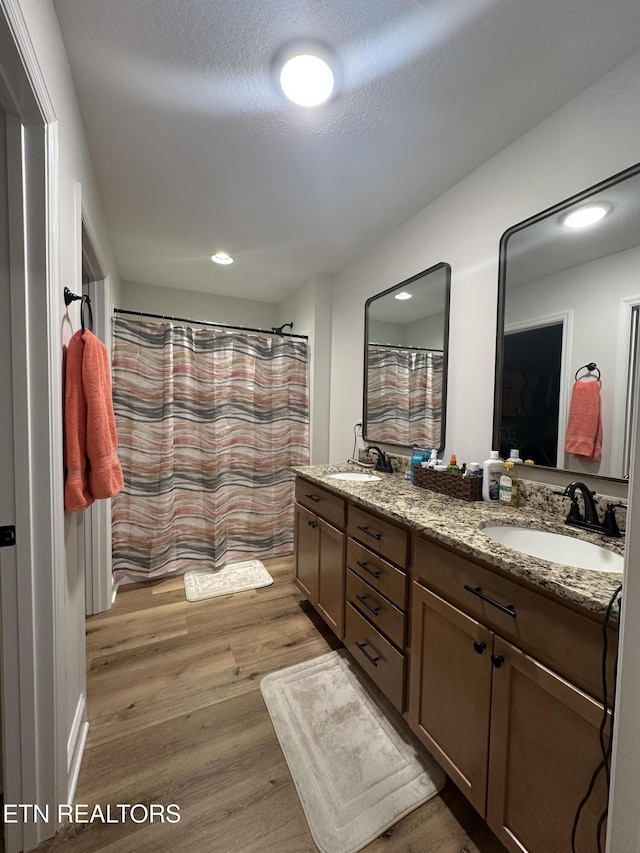 full bathroom with a textured ceiling, double vanity, wood finished floors, and a sink