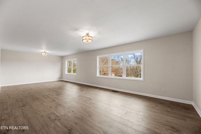 spare room featuring visible vents, baseboards, and dark wood-style flooring