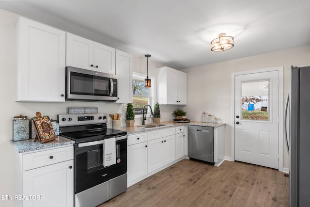 kitchen with a sink, light stone counters, stainless steel appliances, light wood-style floors, and white cabinets