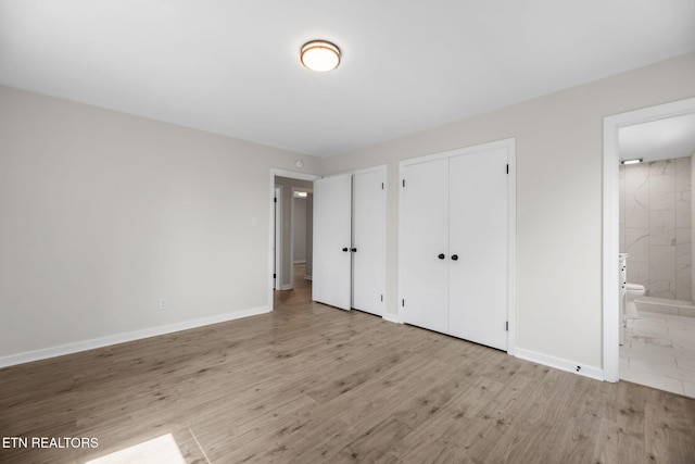 unfurnished bedroom featuring connected bathroom, two closets, baseboards, and wood finished floors