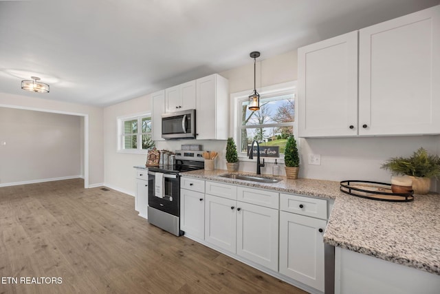 kitchen with baseboards, a sink, stainless steel appliances, white cabinets, and light wood-style floors