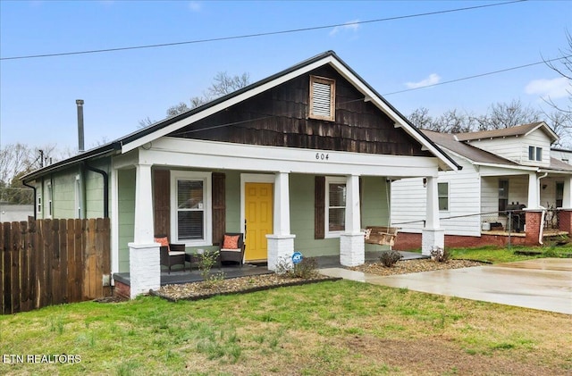 view of front facade featuring covered porch, a front yard, and fence