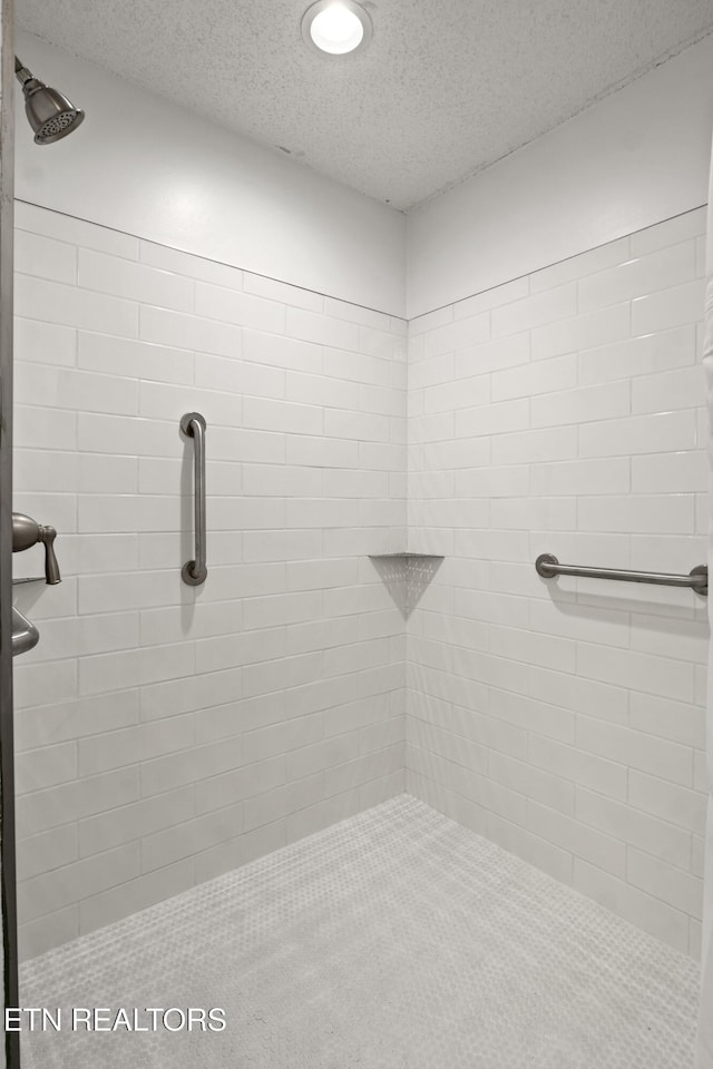 bathroom with a textured ceiling and tiled shower