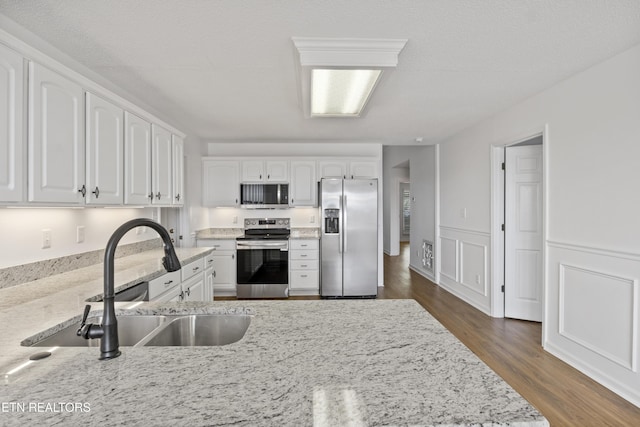 kitchen featuring white cabinetry, light stone countertops, dark wood-type flooring, stainless steel appliances, and a sink