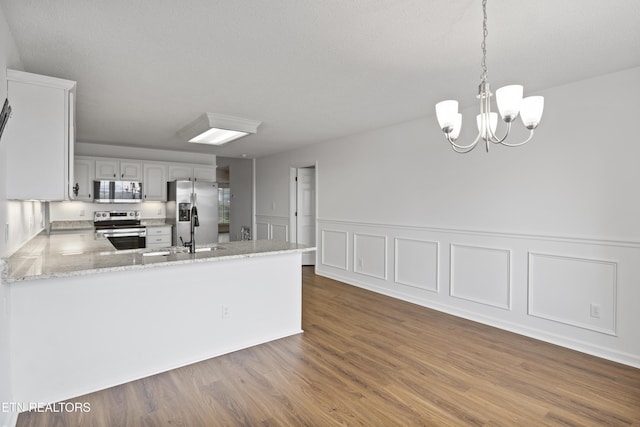 kitchen with light stone countertops, dark wood-type flooring, a peninsula, a sink, and stainless steel appliances