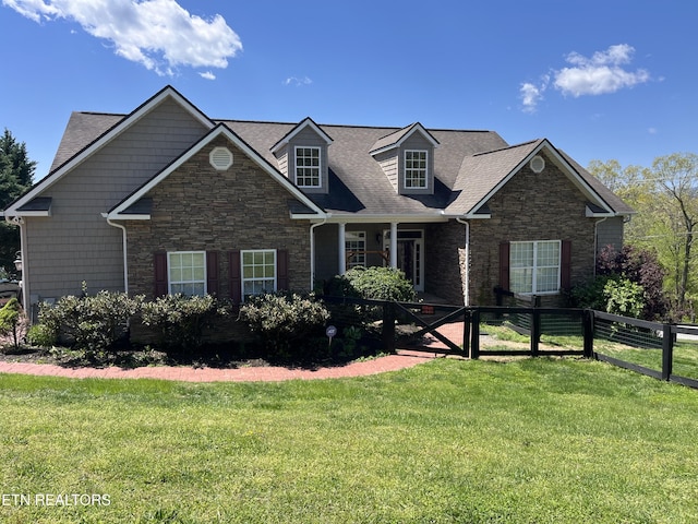 new england style home featuring a shingled roof, stone siding, fence, and a front lawn