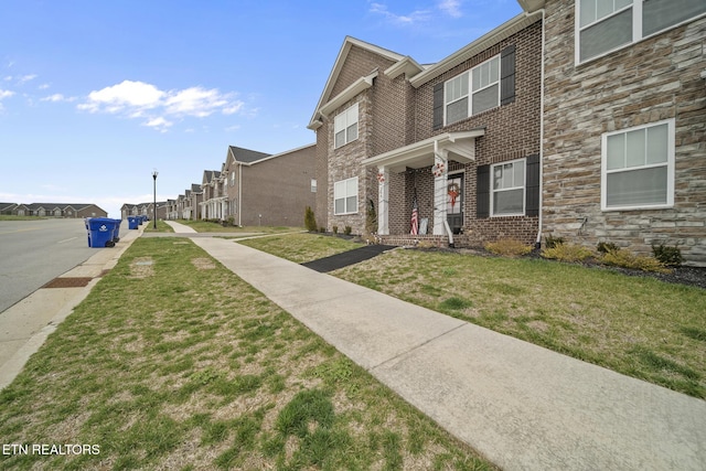 view of front of property featuring stone siding, brick siding, and a front lawn