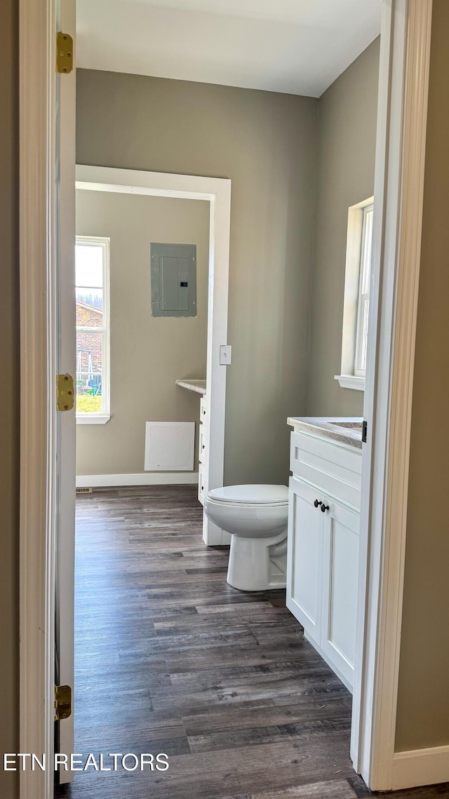 half bath featuring baseboards, toilet, electric panel, wood finished floors, and vanity