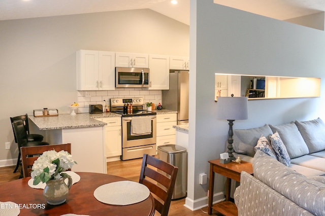 kitchen featuring light wood-type flooring, light stone counters, appliances with stainless steel finishes, white cabinets, and decorative backsplash