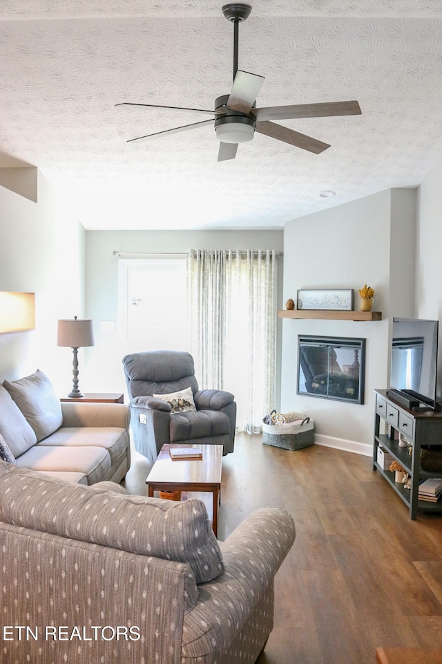 living area featuring a glass covered fireplace, a textured ceiling, wood finished floors, and a ceiling fan