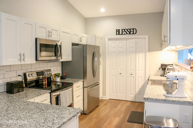 kitchen featuring light stone countertops, stainless steel appliances, light wood-style floors, white cabinetry, and backsplash