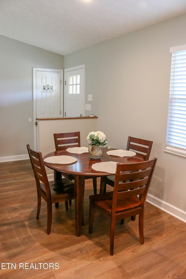 dining space featuring light wood-type flooring, lofted ceiling, and baseboards