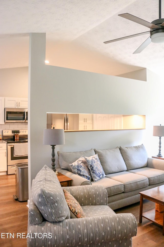 living room with ceiling fan, light wood-style floors, and vaulted ceiling