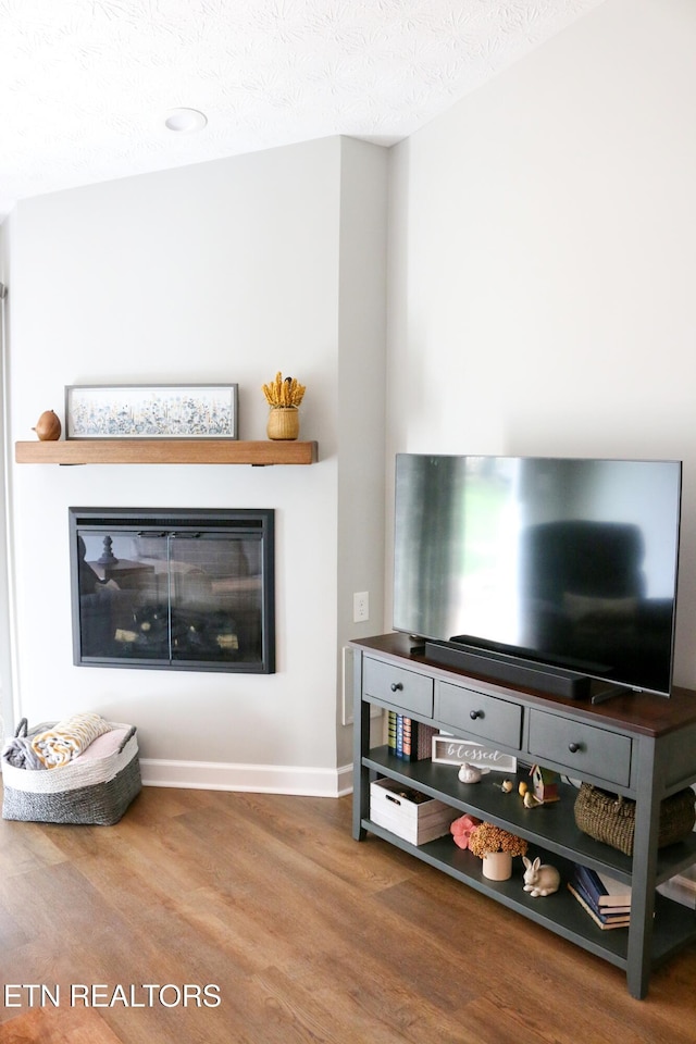 living room featuring a glass covered fireplace, a textured ceiling, baseboards, and wood finished floors