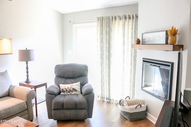 living area with a wealth of natural light, baseboards, wood finished floors, and a glass covered fireplace