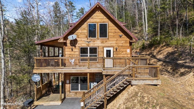 rear view of property with a forest view, a deck, and stairs