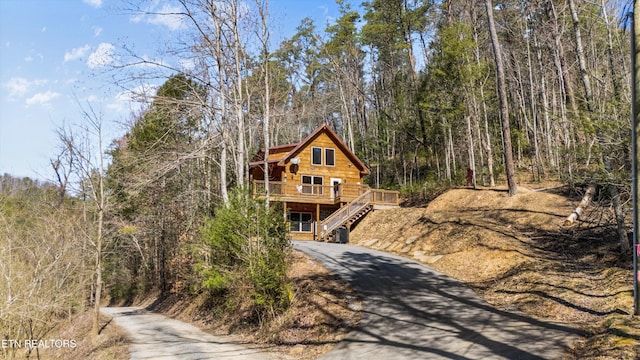 cabin with aphalt driveway, a deck, stairs, and a view of trees
