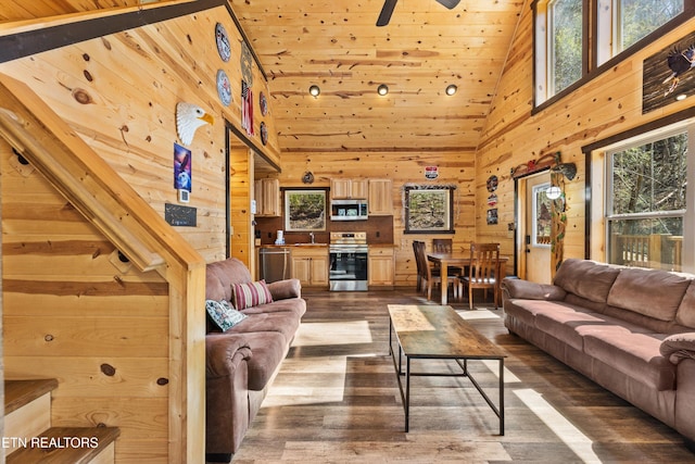 living room featuring wooden walls, dark wood-style flooring, ceiling fan, and high vaulted ceiling