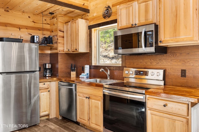 kitchen featuring light brown cabinets, butcher block countertops, a sink, wood walls, and stainless steel appliances