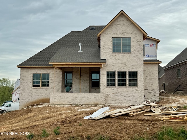 back of property featuring brick siding and roof with shingles