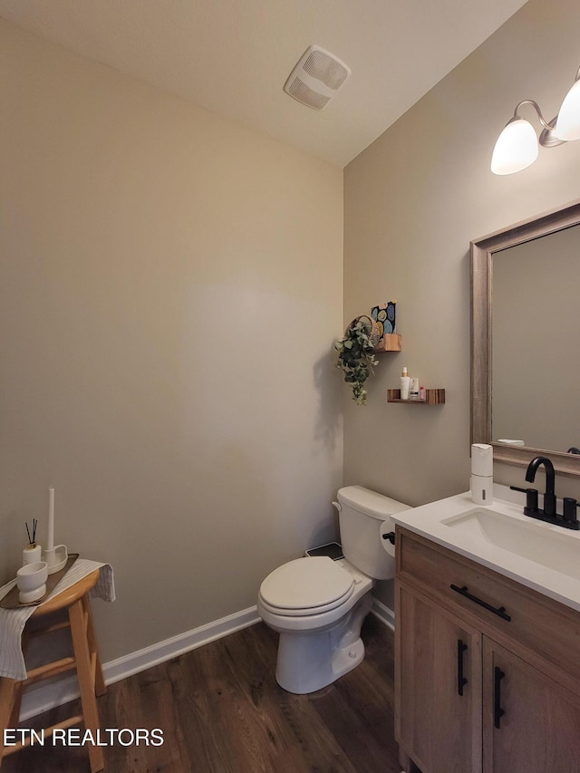 half bathroom with vanity, visible vents, toilet, wood finished floors, and baseboards
