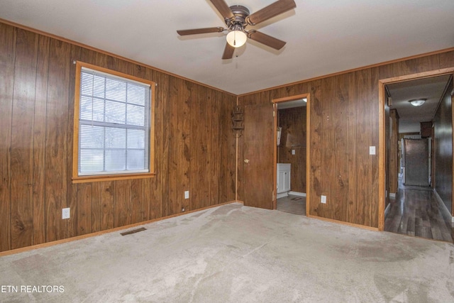 carpeted spare room with crown molding, visible vents, wooden walls, and a ceiling fan
