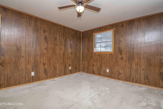 carpeted spare room featuring baseboards, wood walls, and a ceiling fan