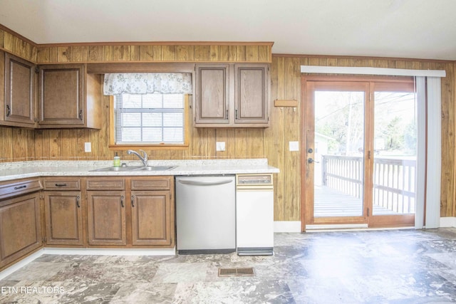 kitchen featuring a sink, wood walls, a healthy amount of sunlight, and stainless steel dishwasher
