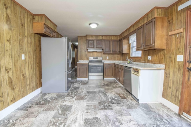 kitchen with light countertops, a sink, wooden walls, appliances with stainless steel finishes, and brown cabinets