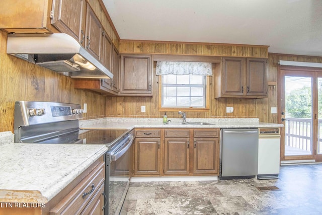 kitchen with light countertops, wooden walls, appliances with stainless steel finishes, a sink, and ventilation hood