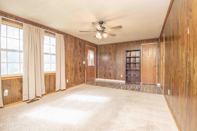 spare room featuring carpet floors, wooden walls, ceiling fan, and visible vents