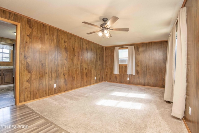 spare room featuring baseboards, a wealth of natural light, wood walls, and a ceiling fan