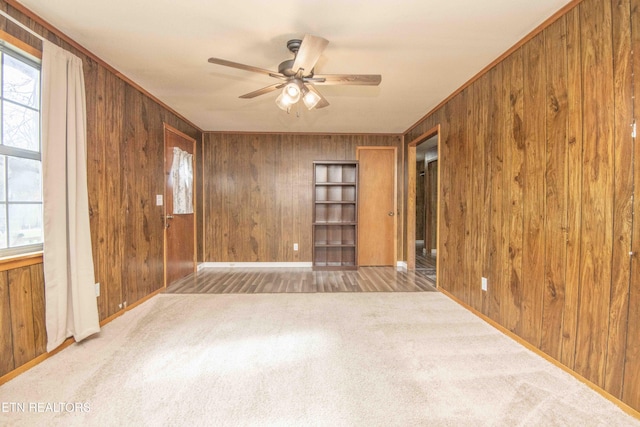 unfurnished room featuring carpet floors, wooden walls, baseboards, ceiling fan, and ornamental molding