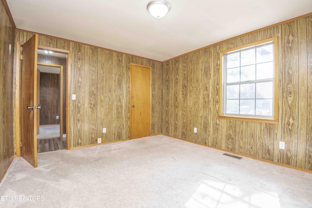 carpeted empty room featuring baseboards, visible vents, and wooden walls