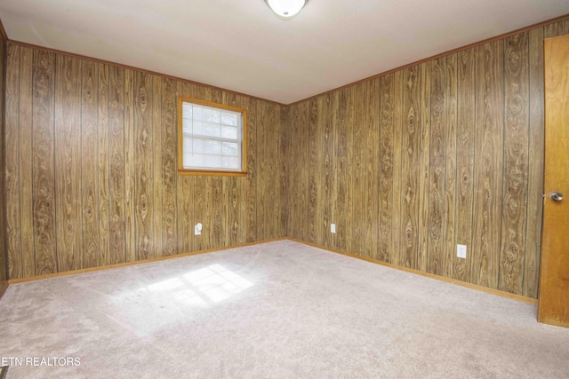 carpeted spare room featuring wood walls and baseboards