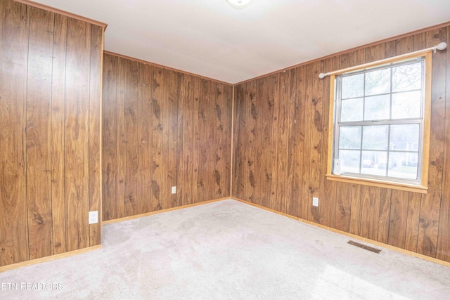 spare room featuring baseboards, visible vents, wood walls, and carpet
