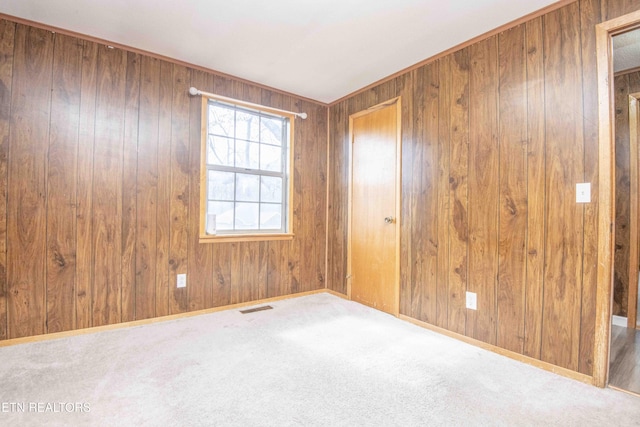 carpeted empty room featuring baseboards, visible vents, and wood walls