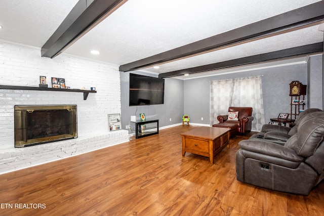 living area with wood finished floors, baseboards, beam ceiling, a textured ceiling, and a brick fireplace